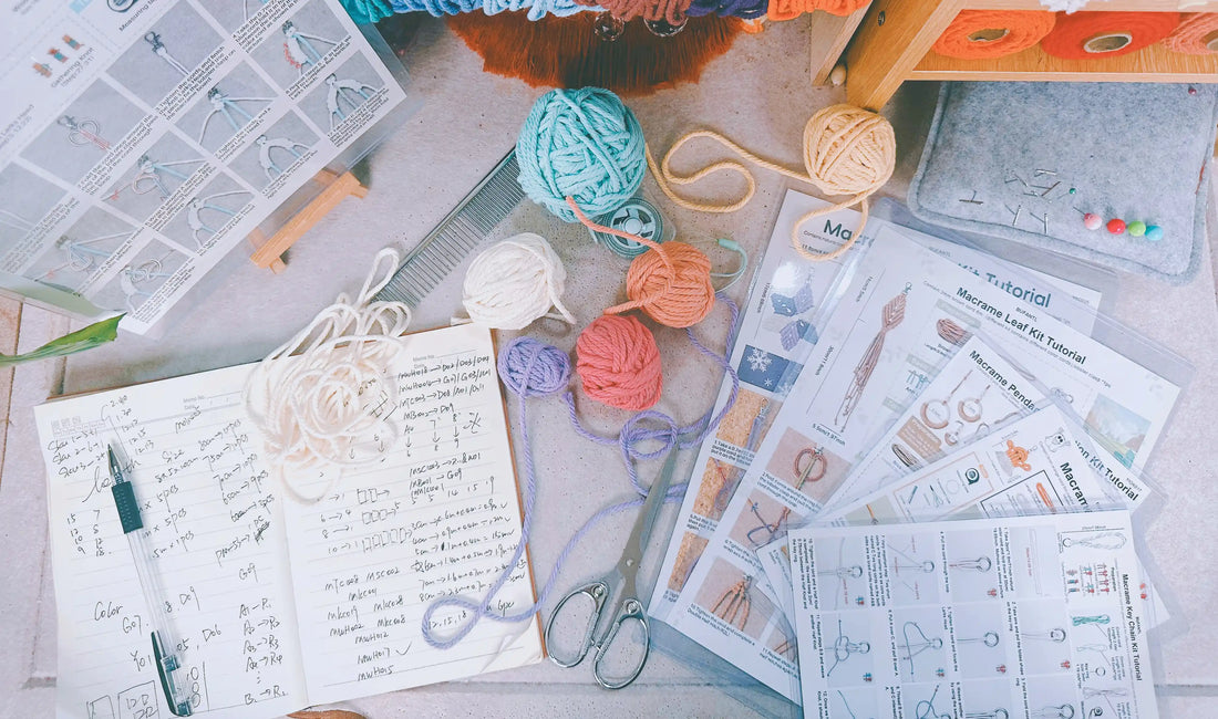 BUFANTL macrame kit development process — planning pages with cord measurements, colour codes and knot counts, surrounded by yarn balls, scissors and printed tutorials